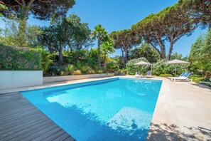 Ein rechteckiger Swimmingpool mit Holzdeck an einer Seite, umgeben von üppiger Vegetation und Bäumen.