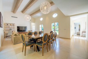 A spacious dining area with a large wooden table and chairs, a television, and a ceiling with wooden beams and pendant lights. - Exceptional country house, Pampelonne and Club 55 just a 3-minute walk away - Pool - Ocean (ramatuelle)