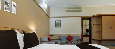 A hotel room with a large bed, a desk with a chair, a sofa, and a wardrobe.