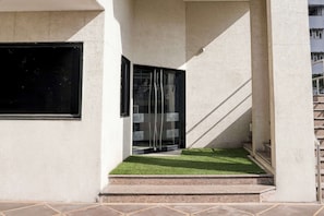 A building entrance with a glass door, a set of stairs leading up to a landing, and a small patch of artificial grass. - Limda Chowk Formerly Hotel Harmony (Rajkot)