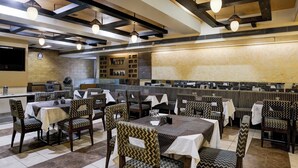 Een restaurant met verschillende eettafels en stoelen, een keukenhoek, en een grote wand met decoratieve details.