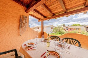 An outdoor dining area with a table set for two, surrounded by chairs, under a wooden pergola. - Appartamento delle Rose by Wonderful Italy (Budoni)