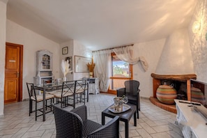A dining area with a table and chairs, a fireplace with pots, and a view through a window. - Appartamento delle Rose by Wonderful Italy (Budoni)