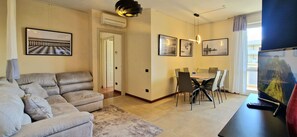 A living room with a sofa, a dining table with chairs, a TV, and framed pictures on the wall. - City / Village Apartment in Viareggio with 2 bedrooms sleeps 4 (Viareggio)