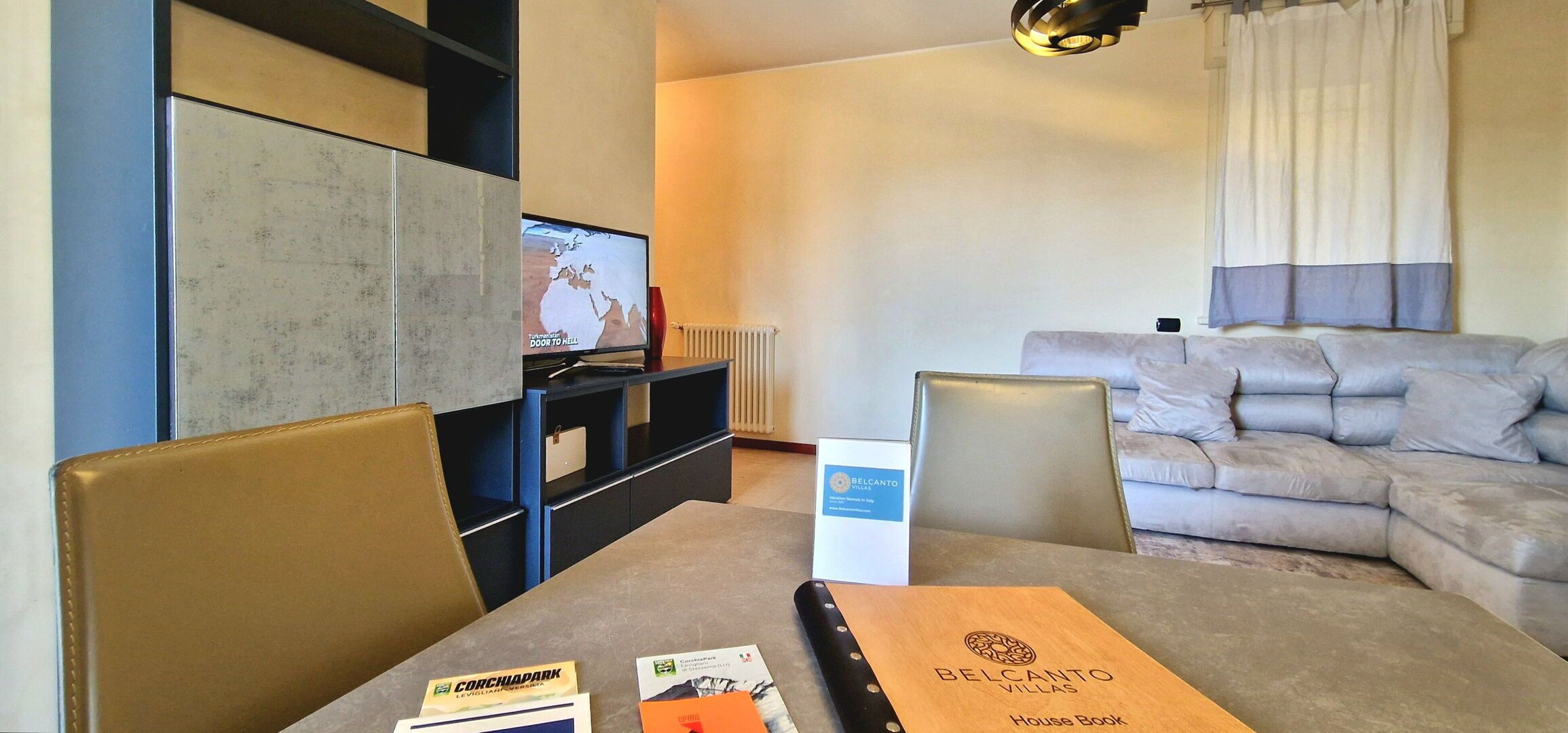 A hotel room with a sofa, a TV, a table with a brochure, and a chair.
