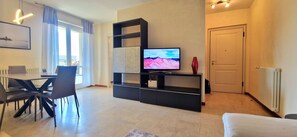 A modern living room with a flat-screen TV, a dining area with chairs, and a door. - City / Village Apartment in Viareggio with 2 bedrooms sleeps 4 (Viareggio)