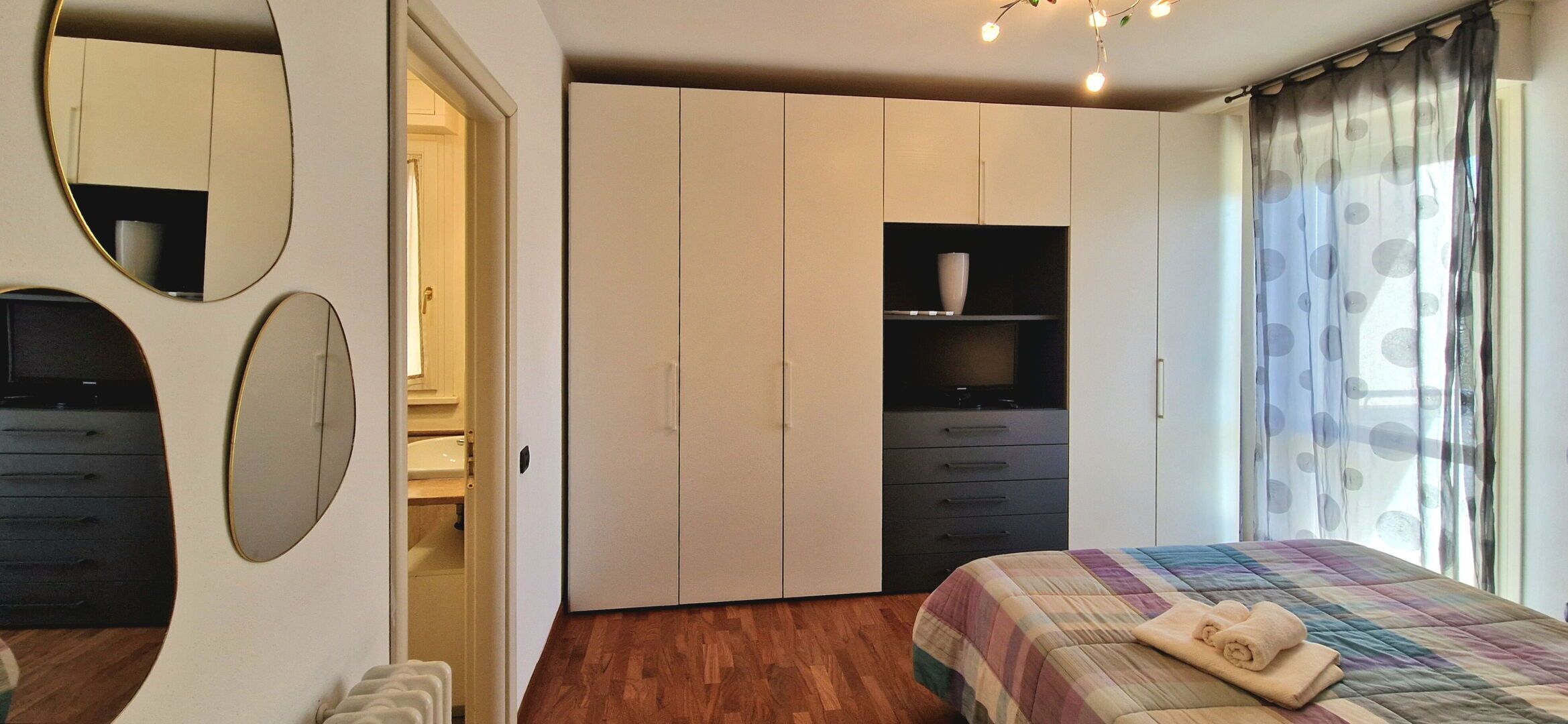 A bedroom with a bed, a wardrobe, a mirror, and a shelf.