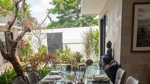 A dining area with a glass table, chairs, and a Buddha statue. - Villa La Casa Ayana Canggu Berawa (Canggu)