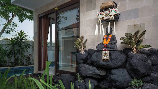 A modern building with a glass door entrance, a stone wall with a Buddha statue, and tropical plants. - Villa La Casa Ayana Canggu Berawa (Canggu)