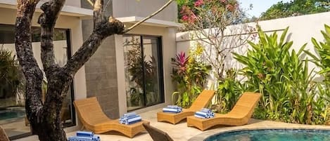 Zona de piscina amb gandules i un arbre.