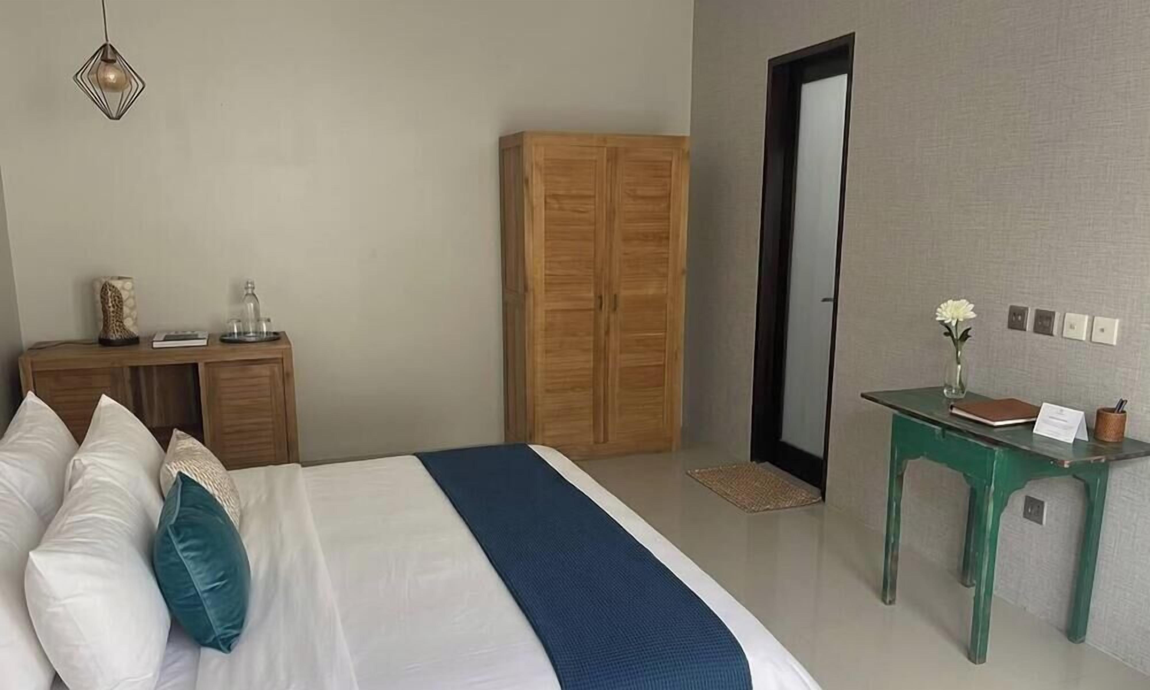 Un dormitorio con cama, armario de madera, una mesita de noche verde y una lámpara colgante.