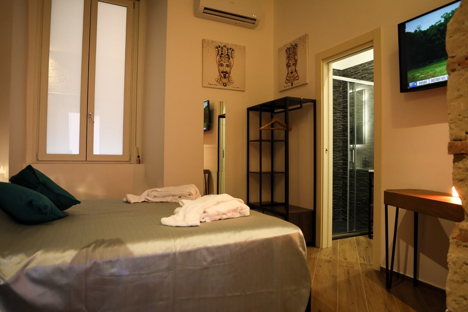 A hotel room with a bed, a TV, a wardrobe, and a bathroom with a glass door.