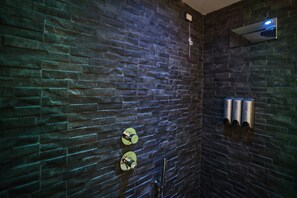 A bathroom with a stone wall, a mirror, a towel dispenser, and a showerhead. - Petramare Charming House: an oasis of wellness and relaxation with a spa in the heart of Salerno (SALERNO)