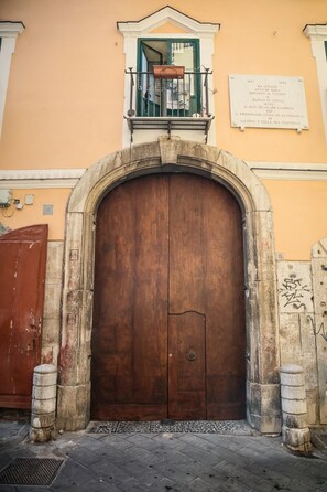 A large wooden door with an arched entrance, flanked by stone pillars, and a small balcony above. - Petramare Charming House: an oasis of wellness and relaxation with a spa in the heart of Salerno (SALERNO)