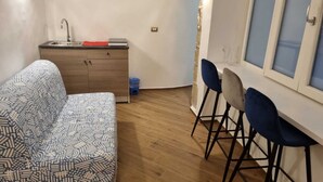 Kompakti oleskelutila, jossa on sohva, pieni keittokomero ja ruokailualue baarituoleineen.