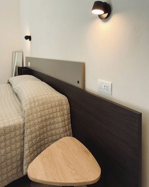 Una habitación de hotel con cama, mesita de noche y lámpara de pared.