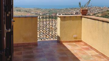 A balcony with a view of a coastal town, a potted plant, and a tiled floor.