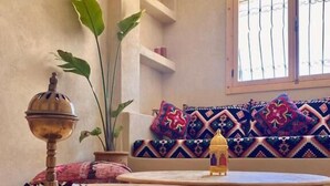 A room with a round wooden table, a patterned sofa, a decorative bowl, and a large window with bars. - Sines Surfmaroc (Aourir)