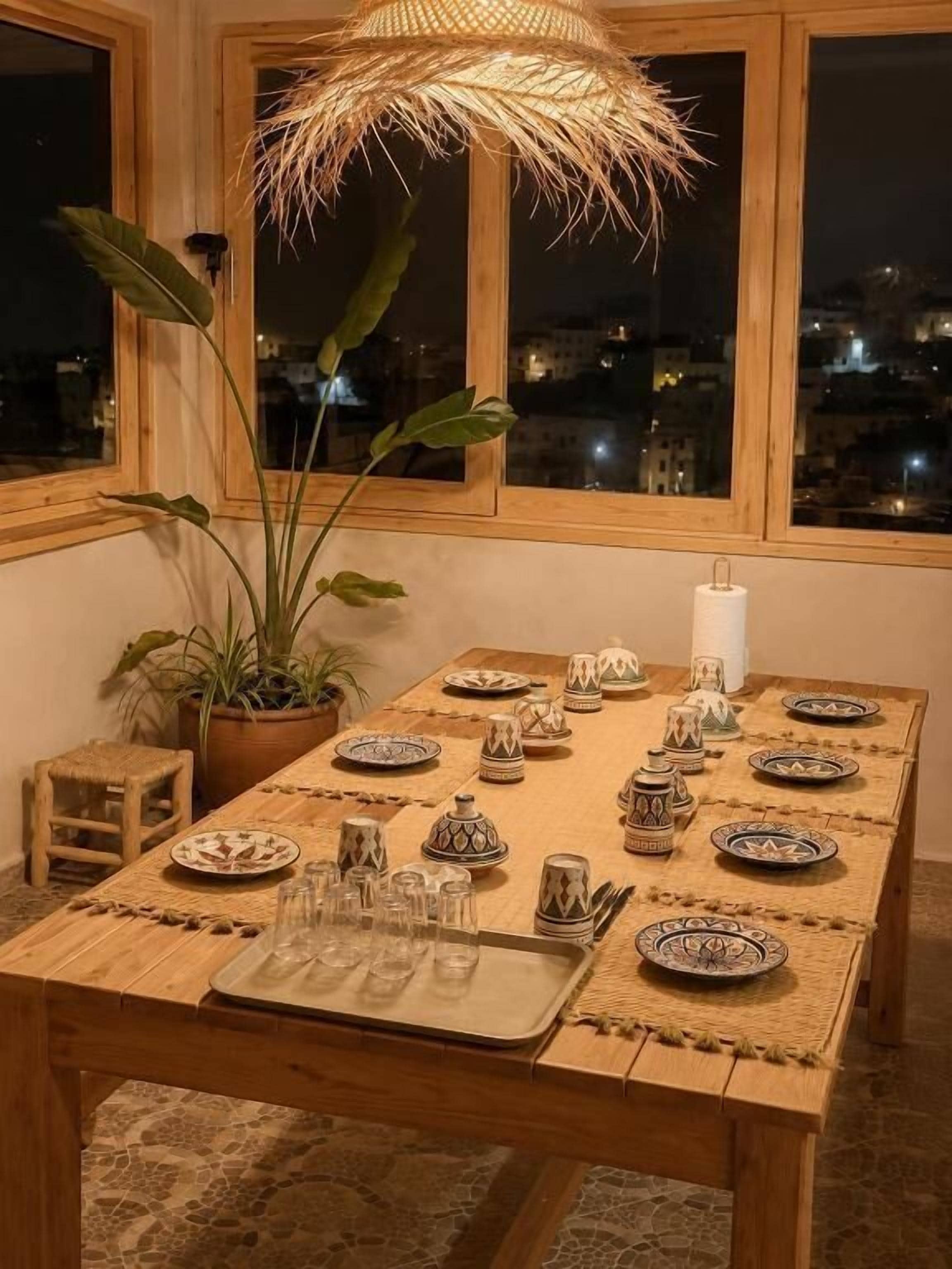 Mesa de comedor lista para seis personas, con platos y vasos con diseños, un mantel tejido y un candelabro.