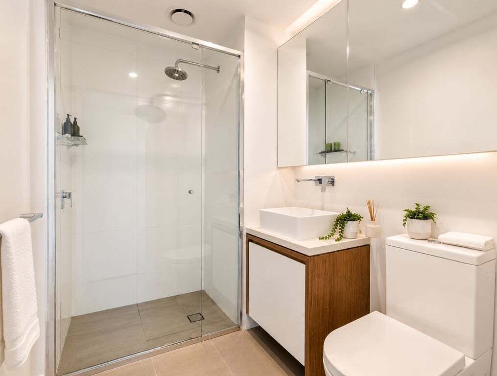 Een moderne badkamer met een douchecabine van glas, een witte wastafel en een grote spiegel.