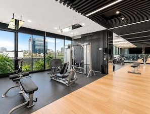 Ein modernes Fitnessstudio mit unterschiedlichen Trainingsgeräten, großen Fenstern und Blick auf die Stadtlandschaft.