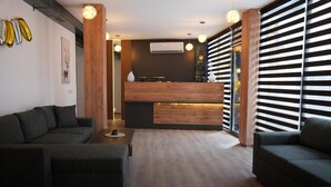 Un interior moderno con una recepción, sofás oscuros y una pared de madera decorativa.