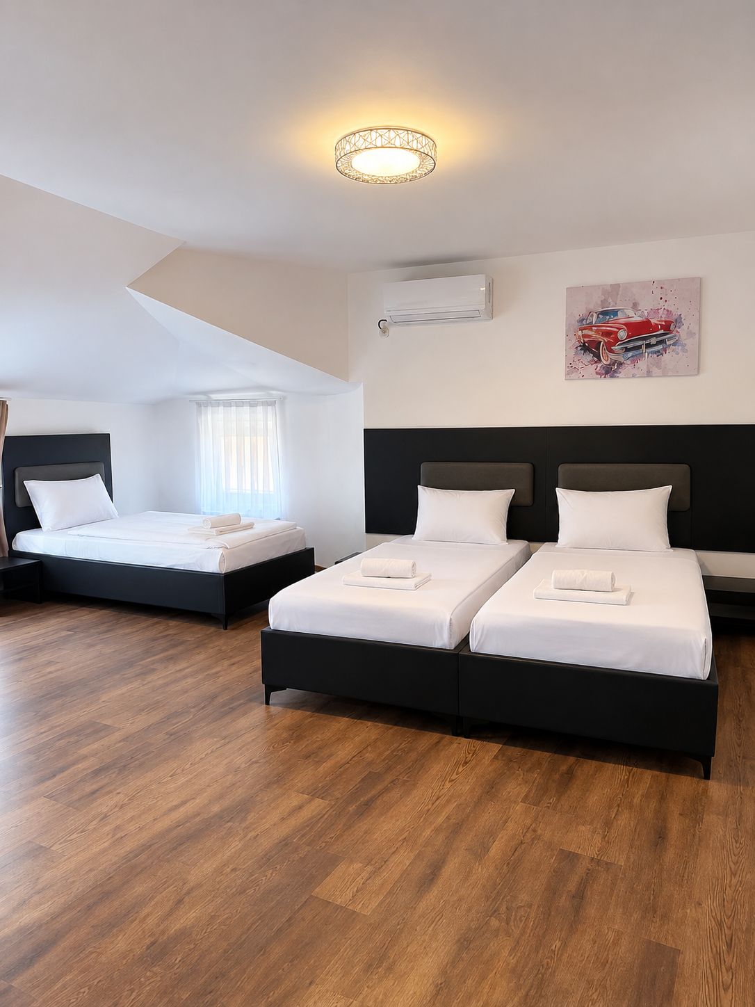Quarto de hotel com duas camas, luminária no teto, aparelho de ar condicionado e uma obra de arte na parede.