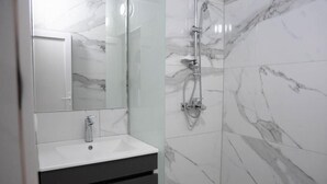 Un bagno con un lavandino bianco, uno specchio e una doccia con pareti in marmo.