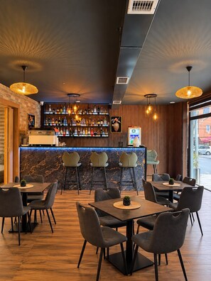 A modern bar area with a marble countertop, multiple bar stools, and a selection of bottles. - Hotel Joana (Prizren)