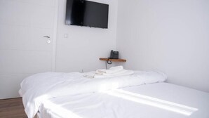 Una camera d'albergo con un letto, una televisione fissata alla parete e un telefono su uno scaffale.