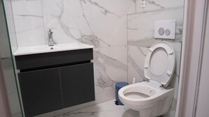 Un baño con inodoro blanco, lavamanos con grifo y un cubo de basura.