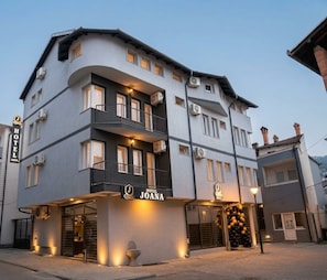 Um hotel com vários andares, com uma placa de destaque para 'Hotel Joana' e varandas nos andares superiores.