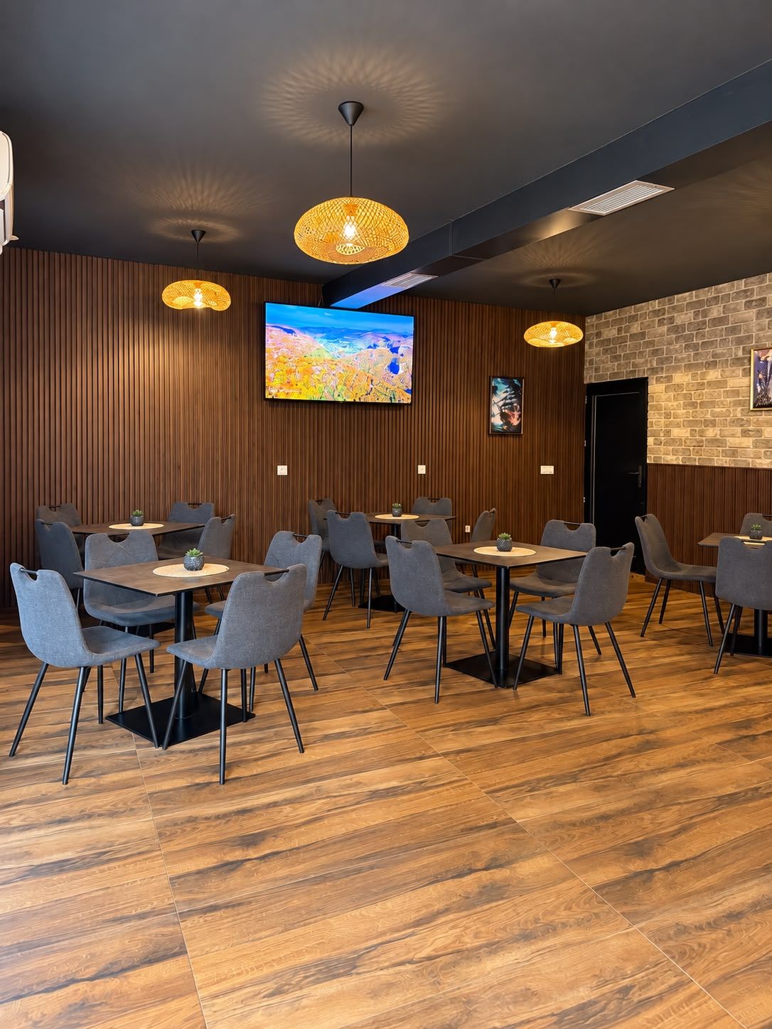 Un espace repas moderne avec des murs lambrissés en bois, un grand téléviseur à écran plat fixé au mur et plusieurs tables accompagnées de chaises.