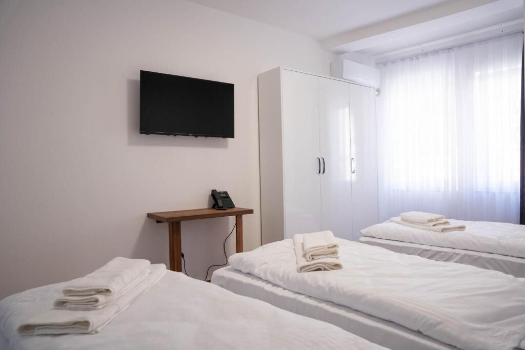 A hotel room with two beds, a TV mounted on the wall, a wardrobe, and a bedside table with a phone.