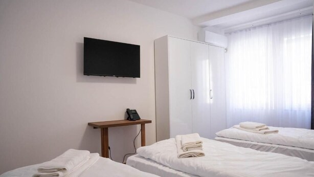 Habitación de hotel con dos camas, un televisor montado en la pared, un armario y una mesita de noche con teléfono.