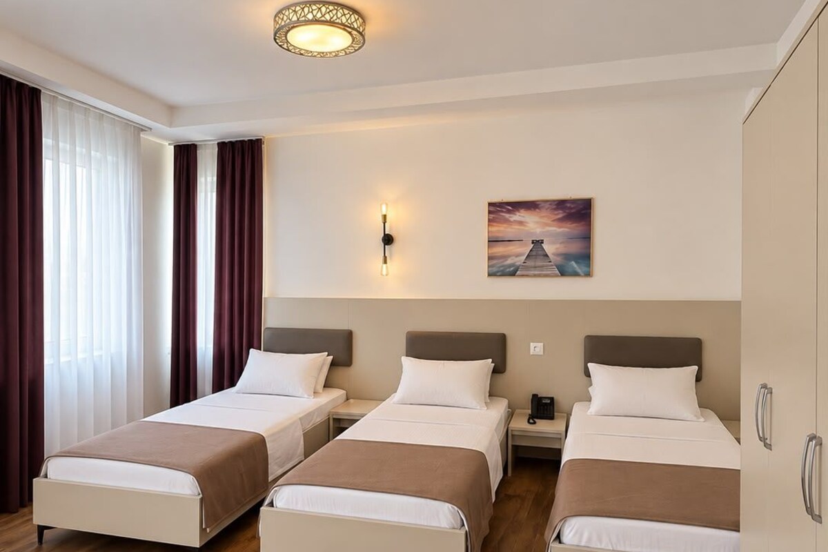A hotel room with three beds, a painting on the wall, and a wooden floor.