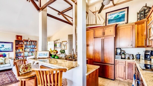 A kitchen with wooden cabinets, a built-in island, and a dining area with a wooden chair and table. - Hale Akala - Huahine (Shared Bathroom) (Kailua-Kona)