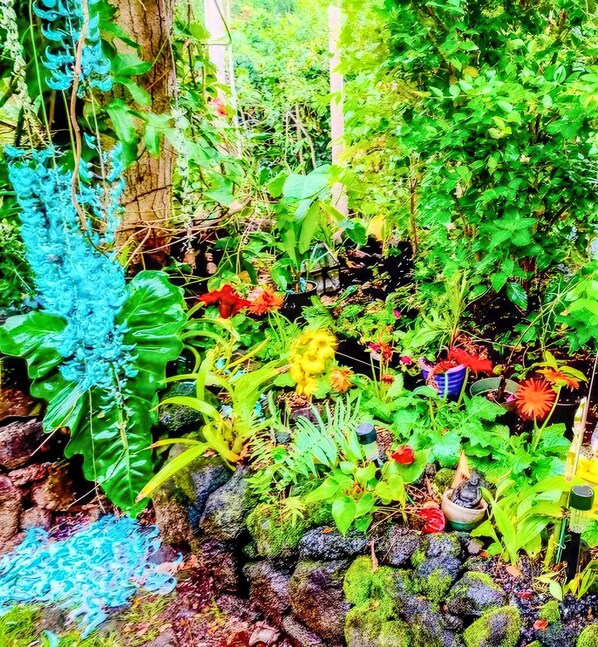 A lush garden with a variety of plants and flowers, a stone wall, and a wooden structure. - Hale Akala - Huahine (Shared Bathroom) (Kailua-Kona)
