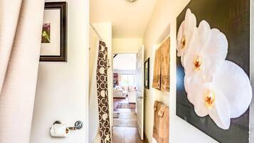 A hallway with a door, a towel rack, and a painting of white flowers.