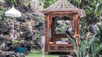 A gazebo with a thatched roof, surrounded by rocks and greenery.