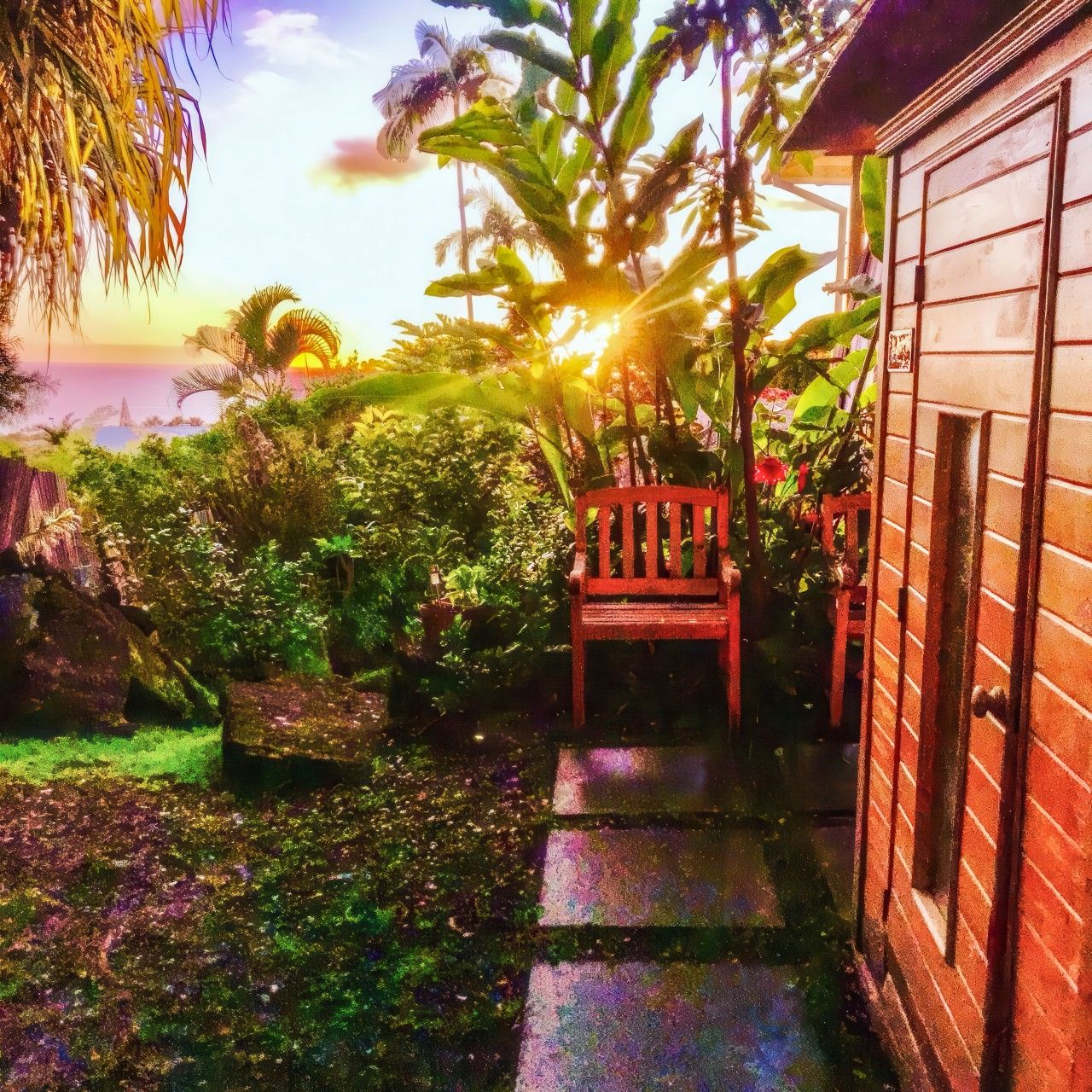 A garden with a wooden chair, a stone bench, and a house with a brick exterior.
