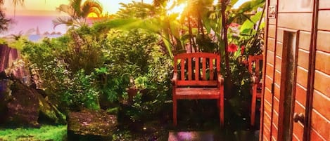 A garden with a wooden chair, a stone bench, and a house with a brick exterior.