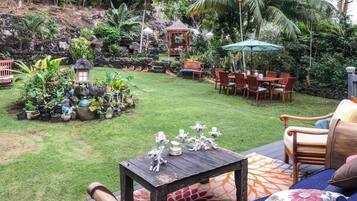 A lush garden with a seating area, a gazebo, and various plants.