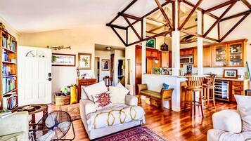 A spacious living room with a large sofa, a dining area with wooden chairs, and a kitchen with wooden cabinets.