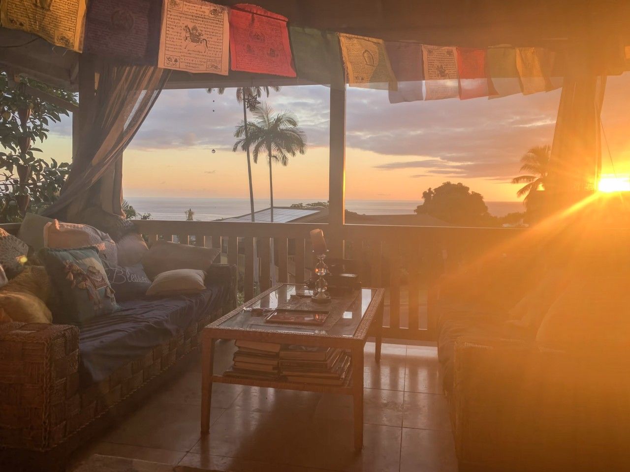 A room with a sofa, a table, and a view of the sunset over the ocean.