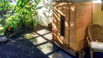 A wooden shed with a door and a window, a wicker chair, and a potted plant in a garden area.