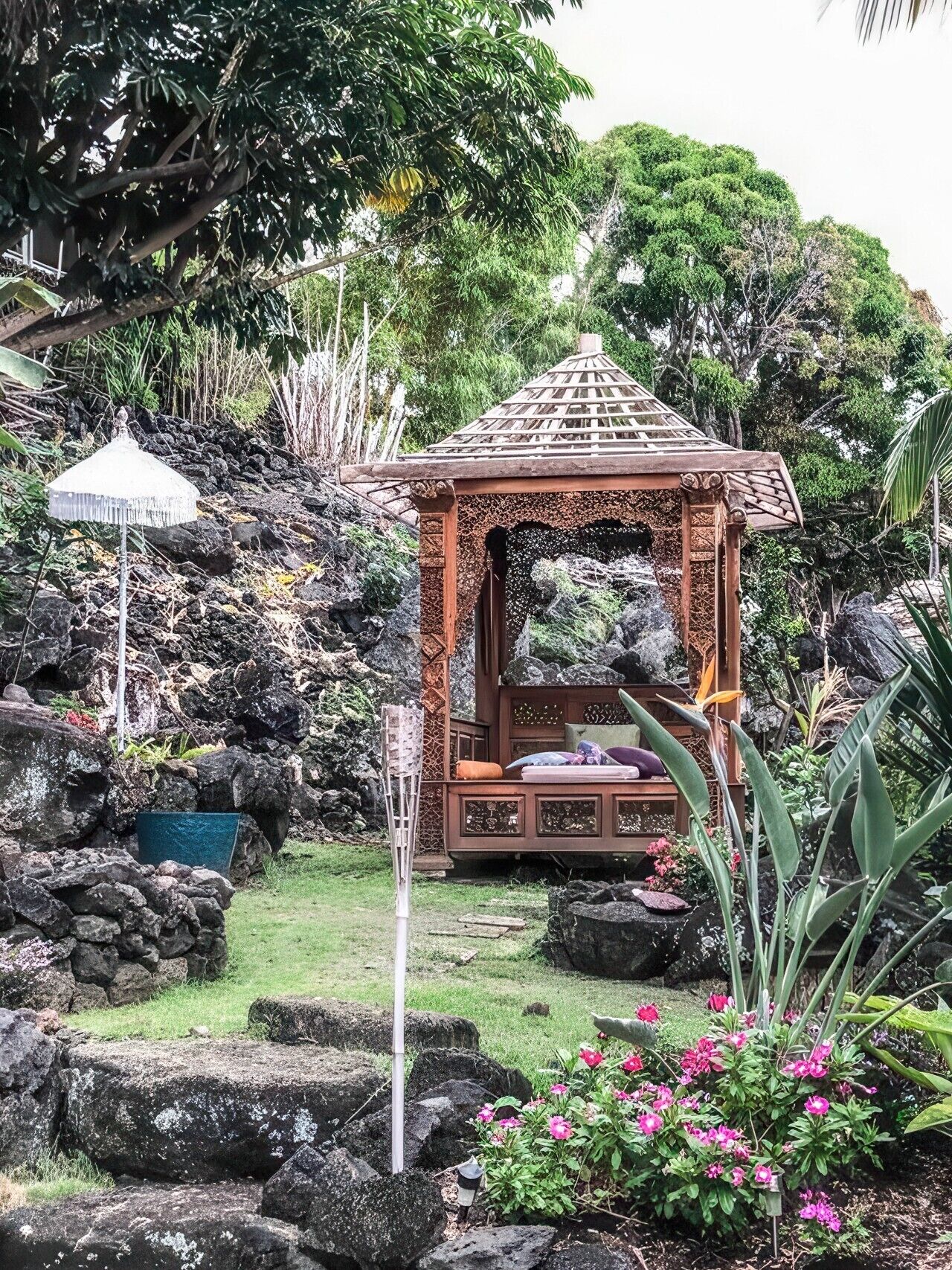 A gazebo with a thatched roof, surrounded by rocks and greenery.