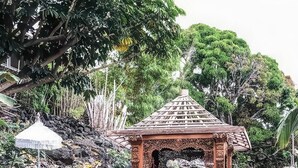 Ein Gartenpavillon mit einem Reetdach, umgeben von Steinen und Grünpflanzen.