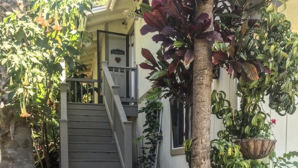 Ein Haus mit Veranda, einer Treppe zum Eingang sowie verschiedenen Blumentöpfen und Blumen.
