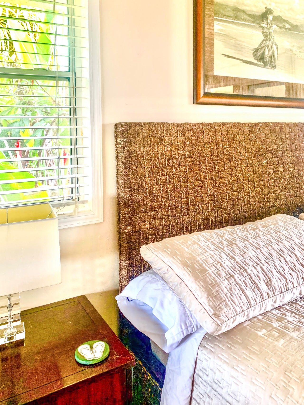 A bedroom with a bed, a nightstand, a window with blinds, and a framed picture on the wall.